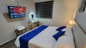 A hotel room with a large bed, a flat-screen TV mounted on the wall, a bedside table with a lamp, and a window with blinds. - Central Apt, Ground Floor, 24h Secure Parking (Durango)
