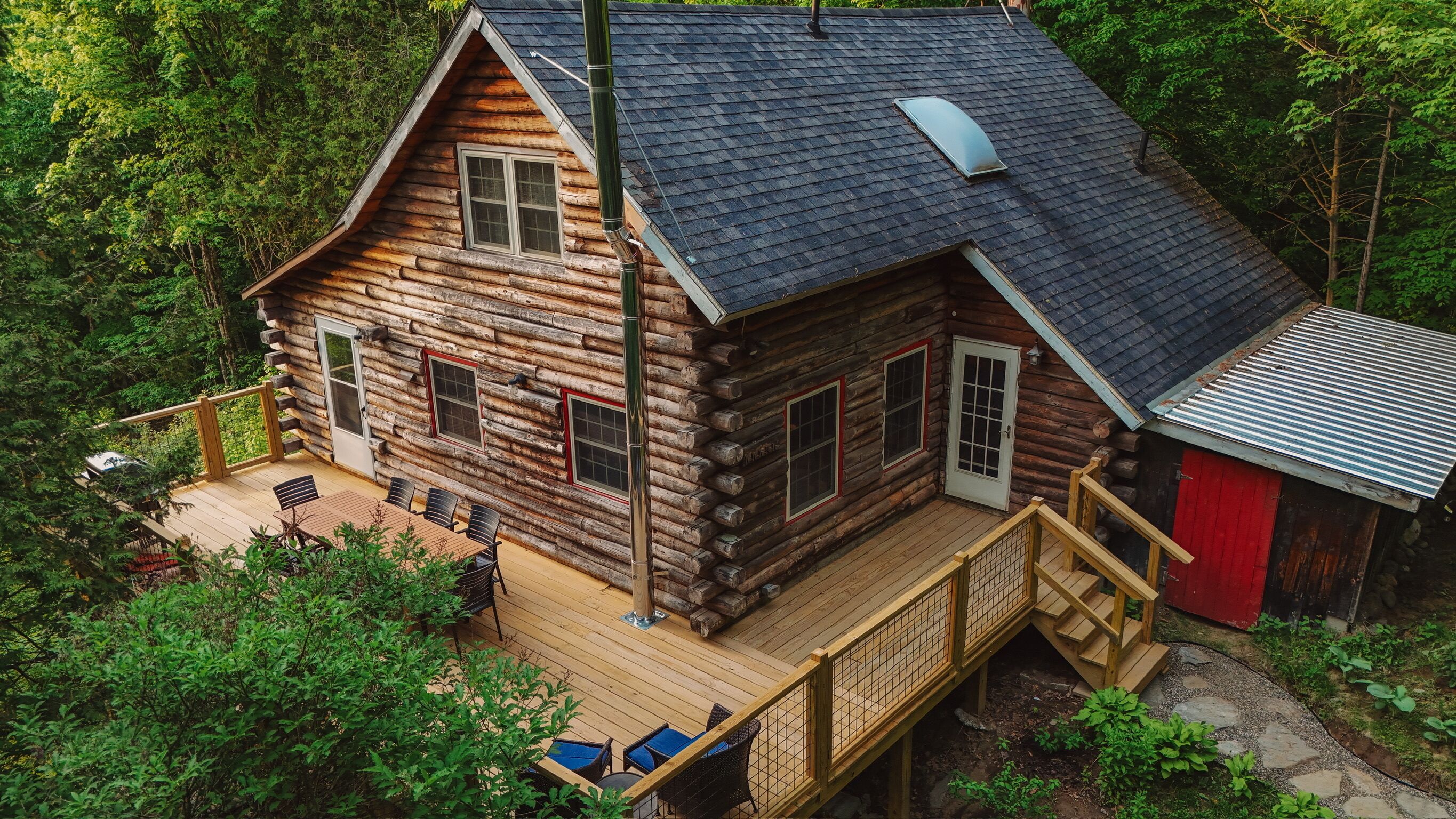 A log cabin with a deck, outdoor seating, and a red shed.