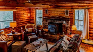 A cozy log cabin interior with a fireplace, leather furniture, and plaid decor. - Rustic Log Cabin w/ Modern Updates - Close to Stowe - Steps from LV Rail Trail (Hyde Park)