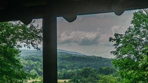 A view from a window with a wooden chair in the foreground, overlooking a lush green landscape with trees and hills. - Rustic Log Cabin w/ Modern Updates - Close to Stowe - Steps from LV Rail Trail (Hyde Park)
