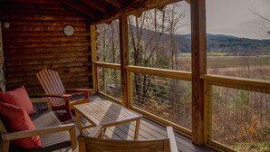 A wooden deck with a view of a forest and hills, furnished with chairs and a table. - Rustic Log Cabin w/ Modern Updates - Close to Stowe - Steps from LV Rail Trail (Hyde Park)