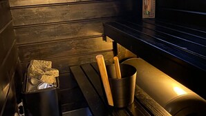 A wooden cabin interior with a window, a sink, a trash bin, and a heater. - Lomariihi 4 (Muurame)