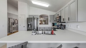 Una cocina moderna con armarios blancos, una isla central, electrodomésticos de acero inoxidable y una lámpara colgante.