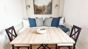 A dining area with a wooden table, four chairs, a bench with cushions, and a framed picture on the wall.