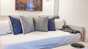 A neatly arranged bedroom with a bed, pillows, a bedside table with a book and a bowl, and a framed picture on the wall.