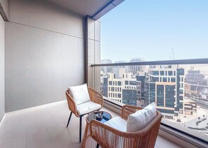 Ein Balkon mit Korbmöbeln, einem Glastisch und Blick auf die Stadt.