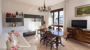 A modern living room with a dining area, a TV, and a chandelier. - At Licia's house (Cuggiono)