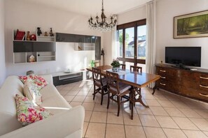 A modern living room with a dining area, a TV, and a chandelier. - At Licia's house (Cuggiono)