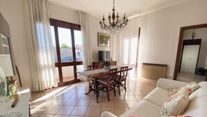 A spacious living room with a dining area, a chandelier, and a view through the glass door. - At Licia's house (Cuggiono)
