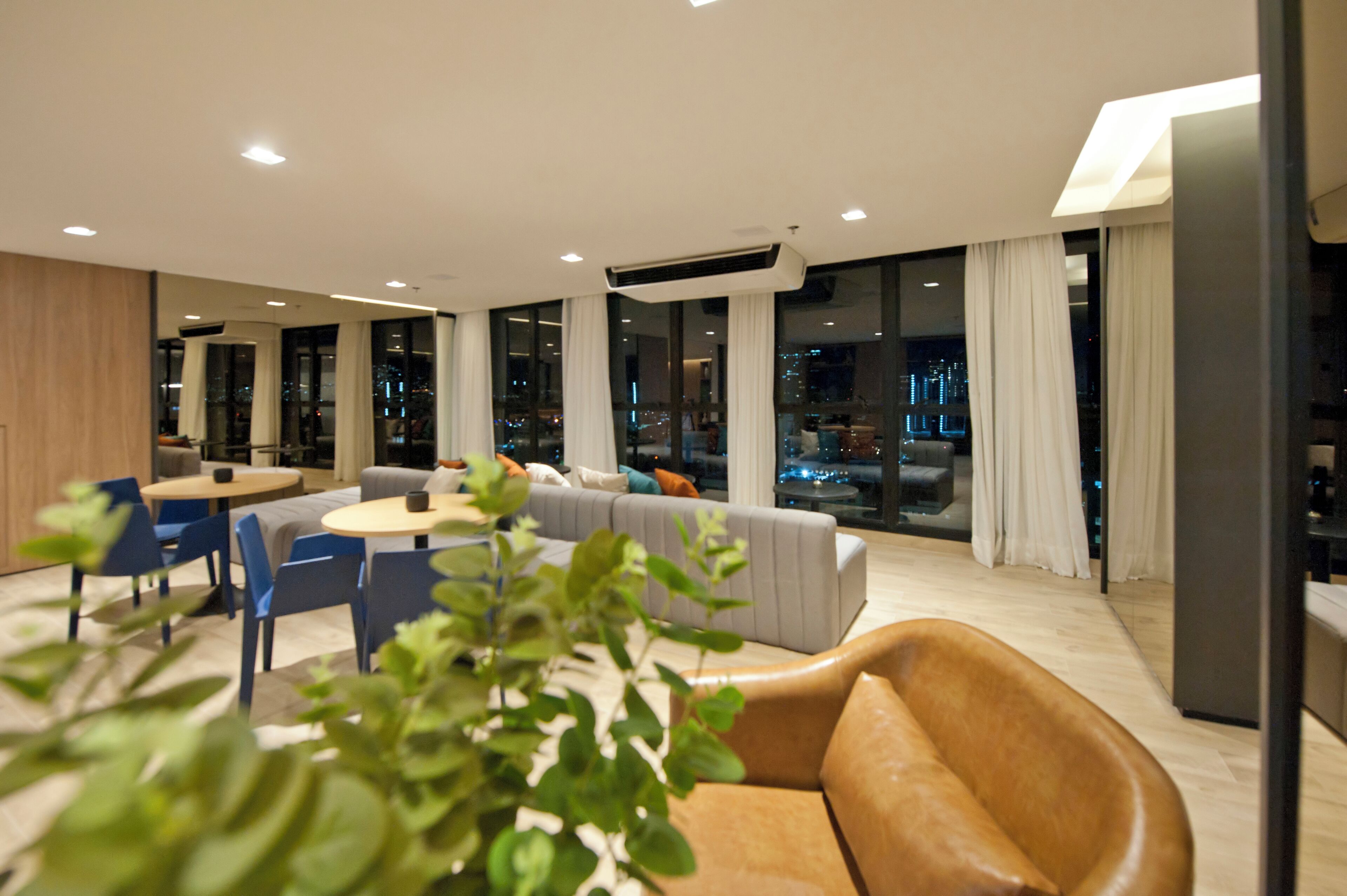A modern living room with a sofa, chairs, a coffee table, and large windows offering a city view.