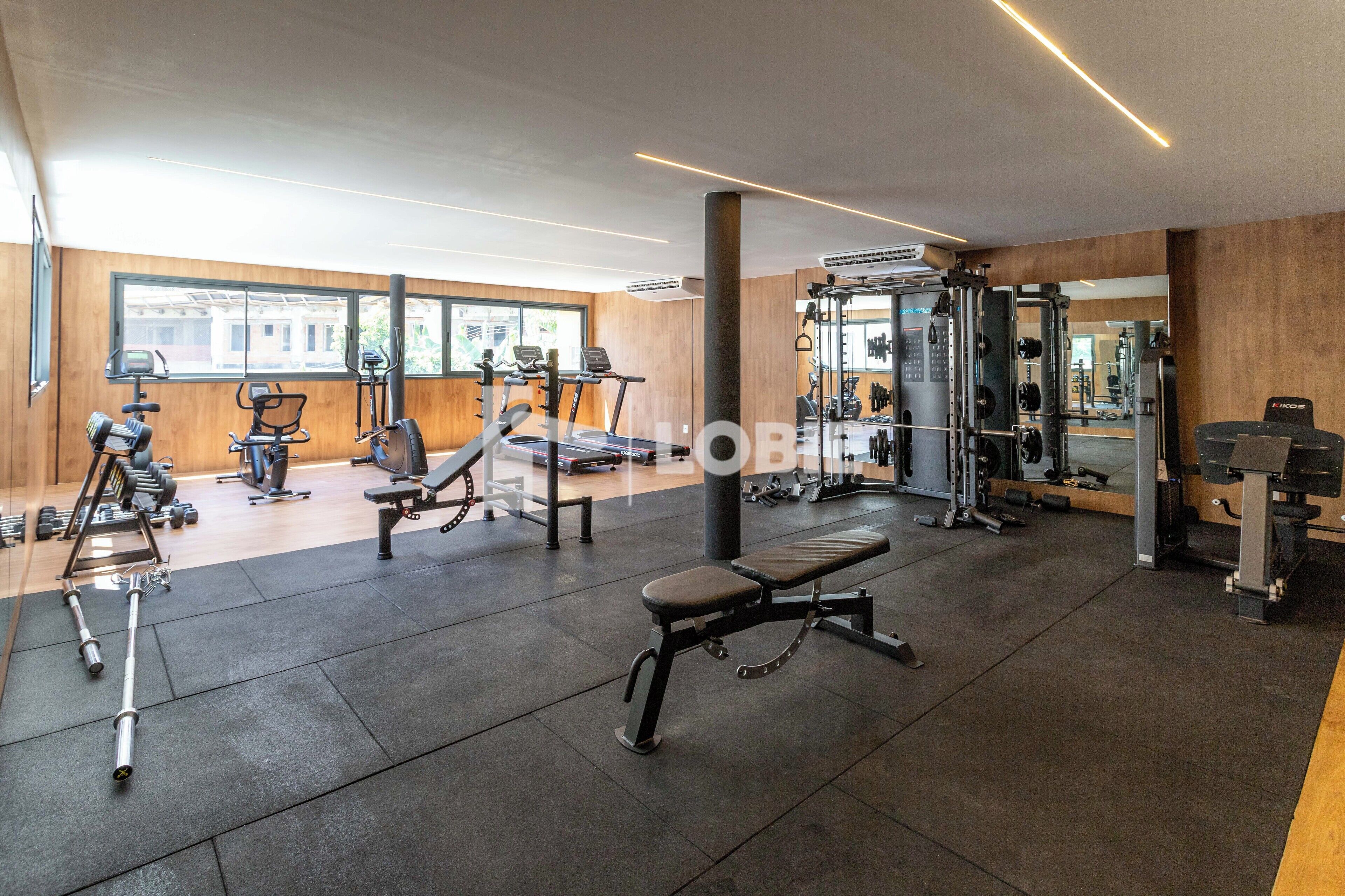A modern gym with various exercise equipment, large windows, and a wooden interior.