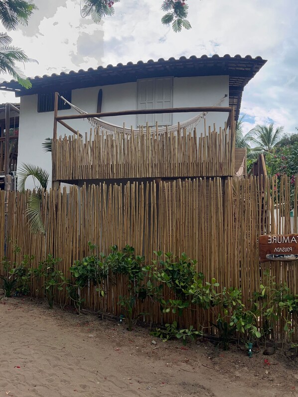 A bamboo fence with a sign reading "PONSADE" in front of a building with a corrugated metal roof. - POUSADA TAMURE (Porto Seguro)