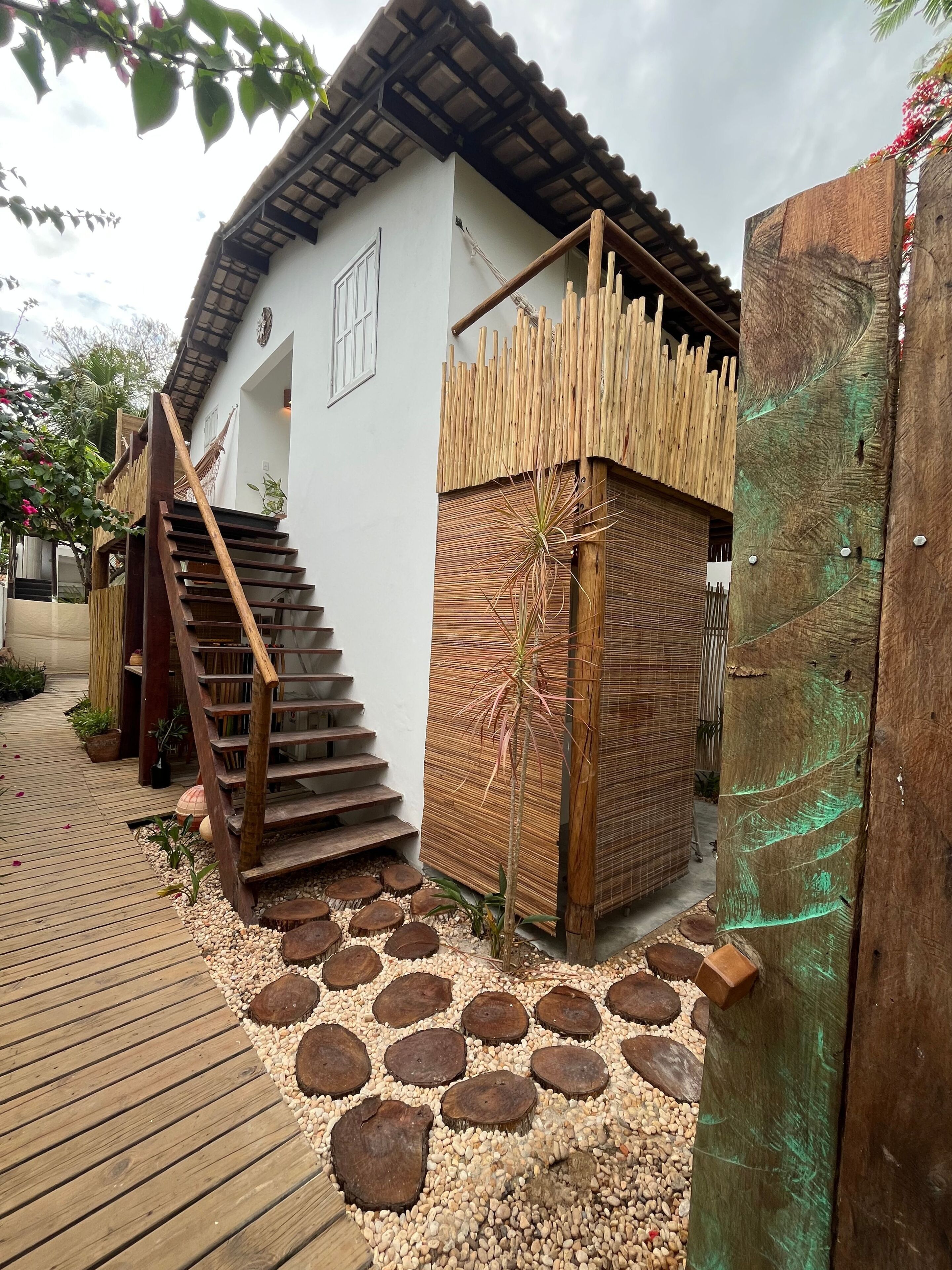 A wooden staircase leading to a white building with a bamboo fence and a small garden area with pebbles and plants.