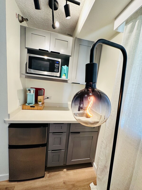 A compact kitchen with a microwave, toaster, and a hanging light fixture.