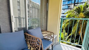 Ein Balkon mit Korbmöbeln und einem Glastisch, mit Blick auf ein Gebäude und Palmen.