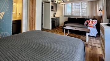 Ein modernes Schlafzimmer mit einem großen Bett, einem kleinen Tisch, einer Couch und einer Küchenzeile im Hintergrund.