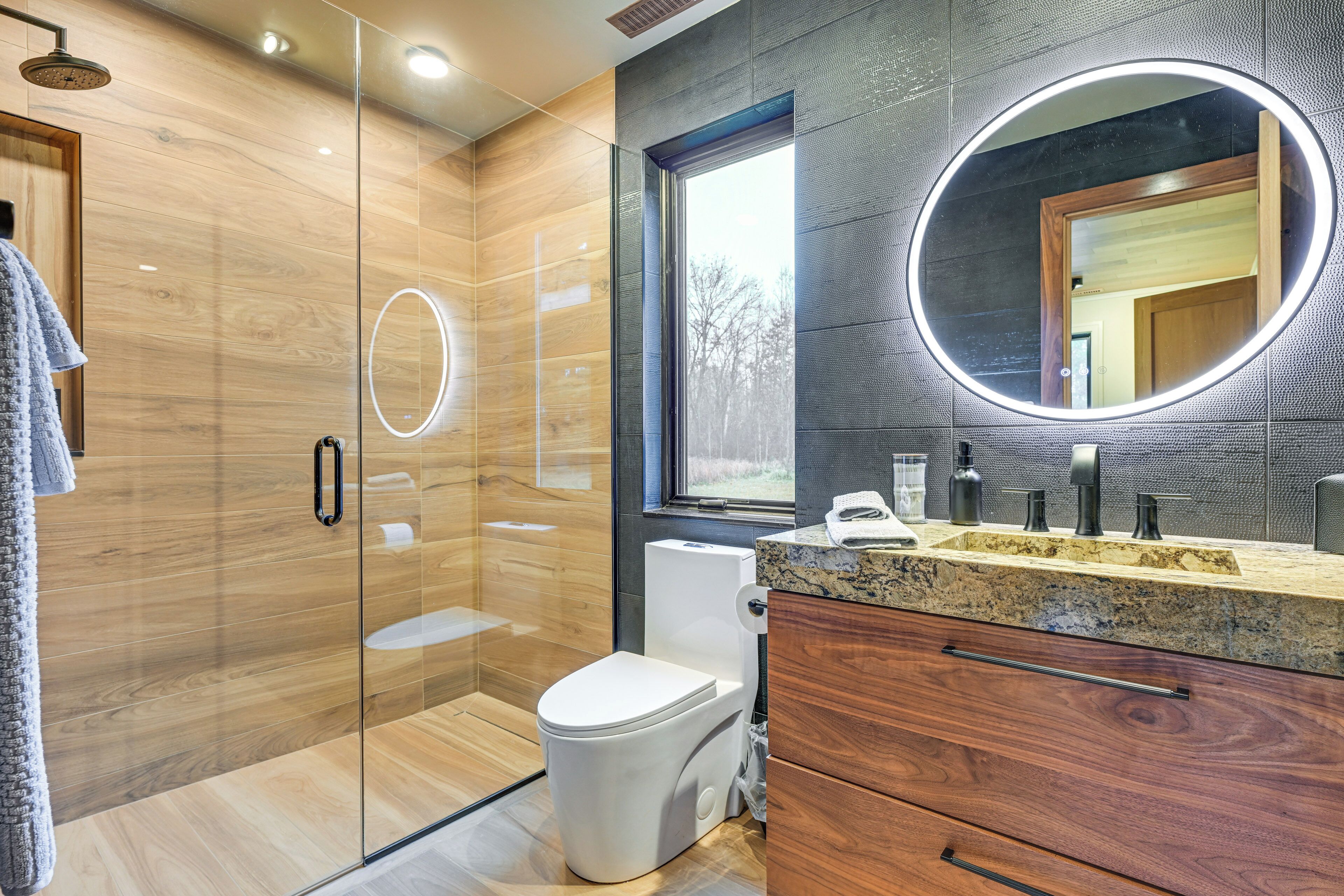 A modern bathroom with a glass-enclosed shower, a toilet, and a vanity with a mirror.