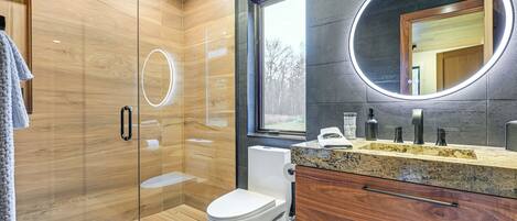 A modern bathroom with a glass-enclosed shower, a toilet, and a vanity with a mirror.