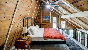 Quarto com teto de madeira, cama com cobertor vermelho, mesa de cabeceira e ventilador de teto.