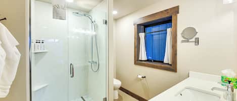 A bathroom with a glass-enclosed shower, a sink with a mirror, and a toilet.