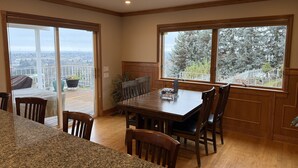 Un comedor con una mesa y sillas de madera, vista a un balcón con baranda y un amplio ventanal con vistas a árboles y una valla.