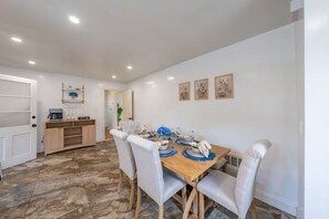 A dining area with a wooden table, white upholstered chairs, and a coffee station. - Spring Getaway Hot Tub, HDTV, Game Room & Parking (Linden)