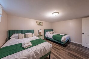 A room with two beds, a bedside table with a lamp, a ceiling light, and a door. - Spring Getaway Hot Tub, HDTV, Game Room & Parking (Linden)