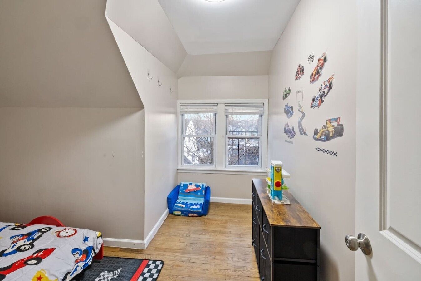 A child's bedroom with a bed, dresser, windows, and wall decals.
