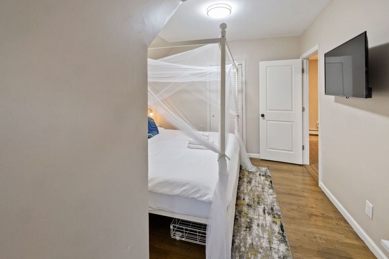 Un dormitorio con una cama con dosel, un televisor montado en la pared y una puerta que da a otra habitación.