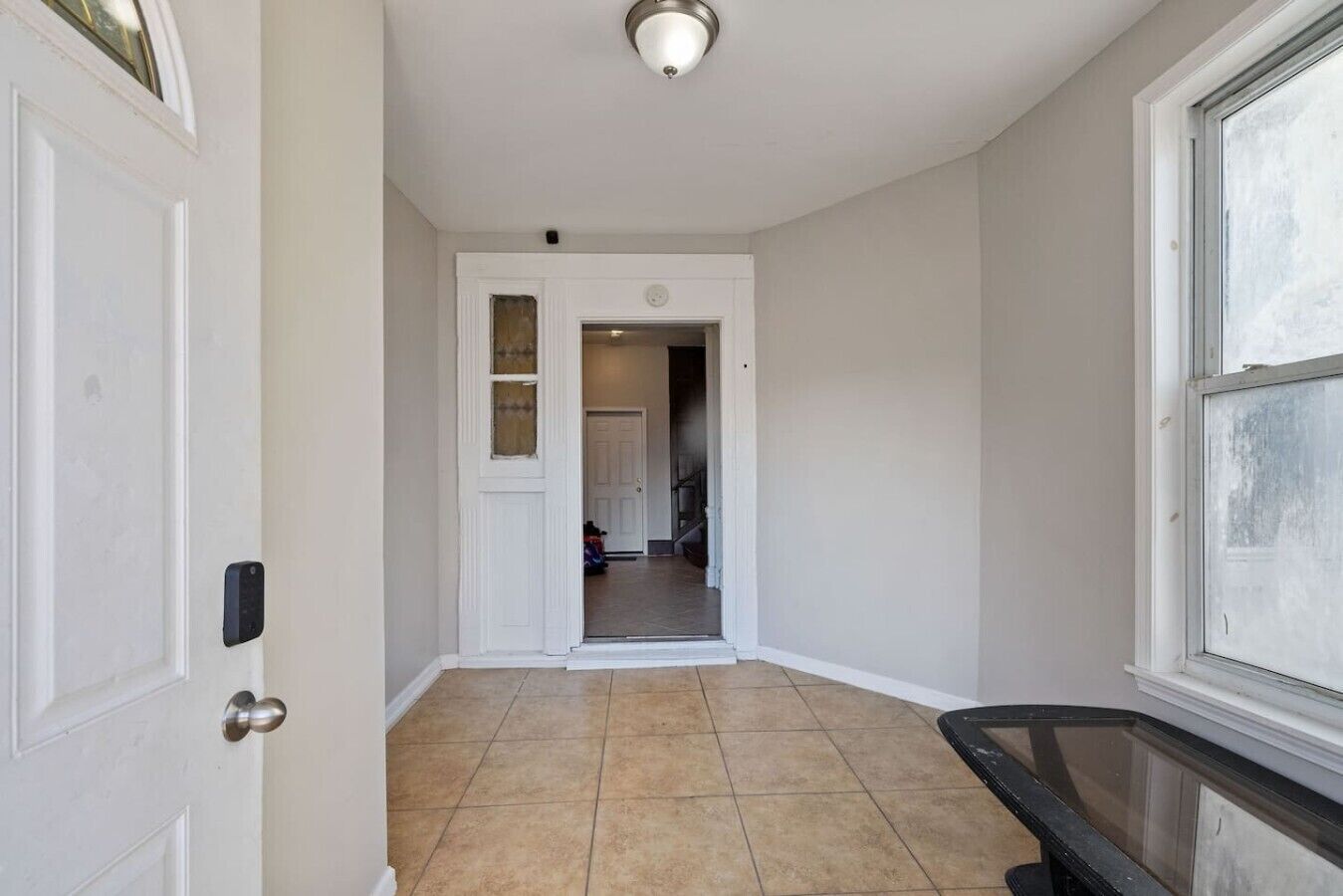 A hallway with a white door, a window, and a tiled floor.