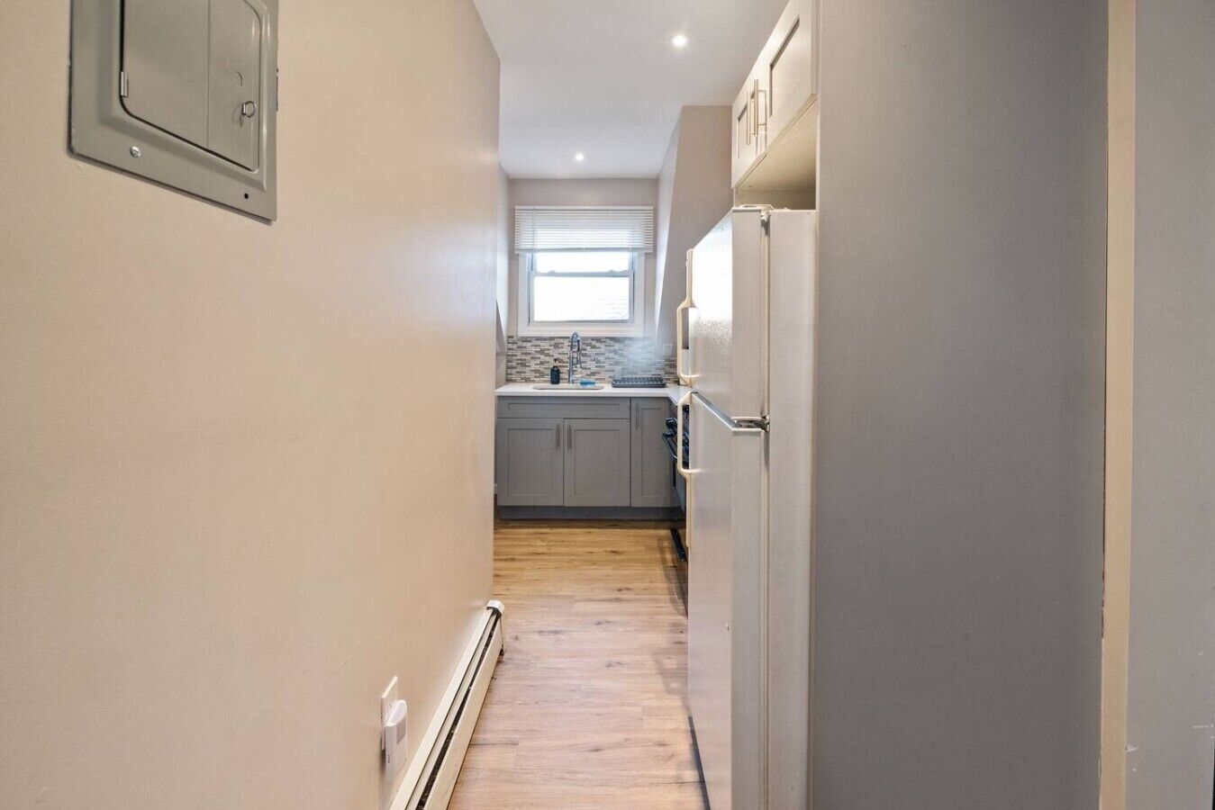 Un pasillo estrecho que da a una cocina con ventana, un radiador y una puerta.