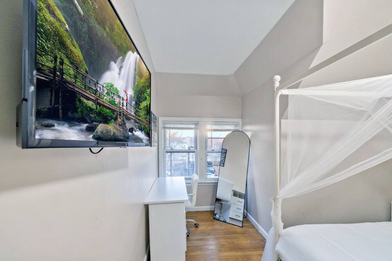 Een slaapkamer met een aan de muur bevestigde televisie, een hemelbed, een bureau en een raam met uitzicht op een waterval.