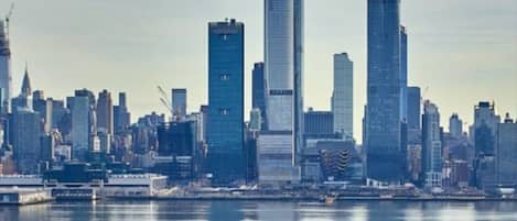A city skyline with modern high-rise buildings, a waterfront, and a road with vehicles.