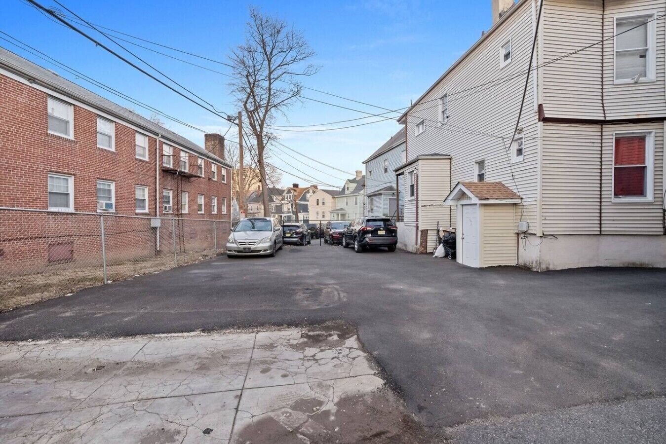 Uma rua estreita, com edifícios residenciais, um carro estacionado e calçada visível.