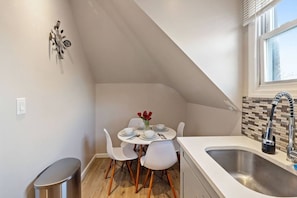 A kitchen with a dining table set for two, a sink, and a window with blinds. - Stylish Newark 2BR | Great WFH, WiFi, Near Transit (East Orange)