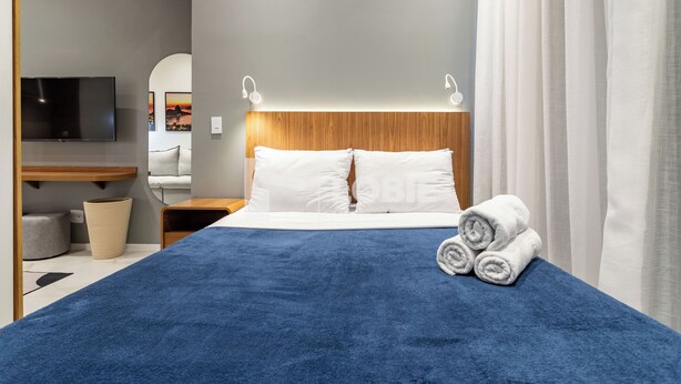 Habitación de hotel con una cama grande, un televisor montado en la pared, cabecera de madera y vistas a la ciudad por la ventana.