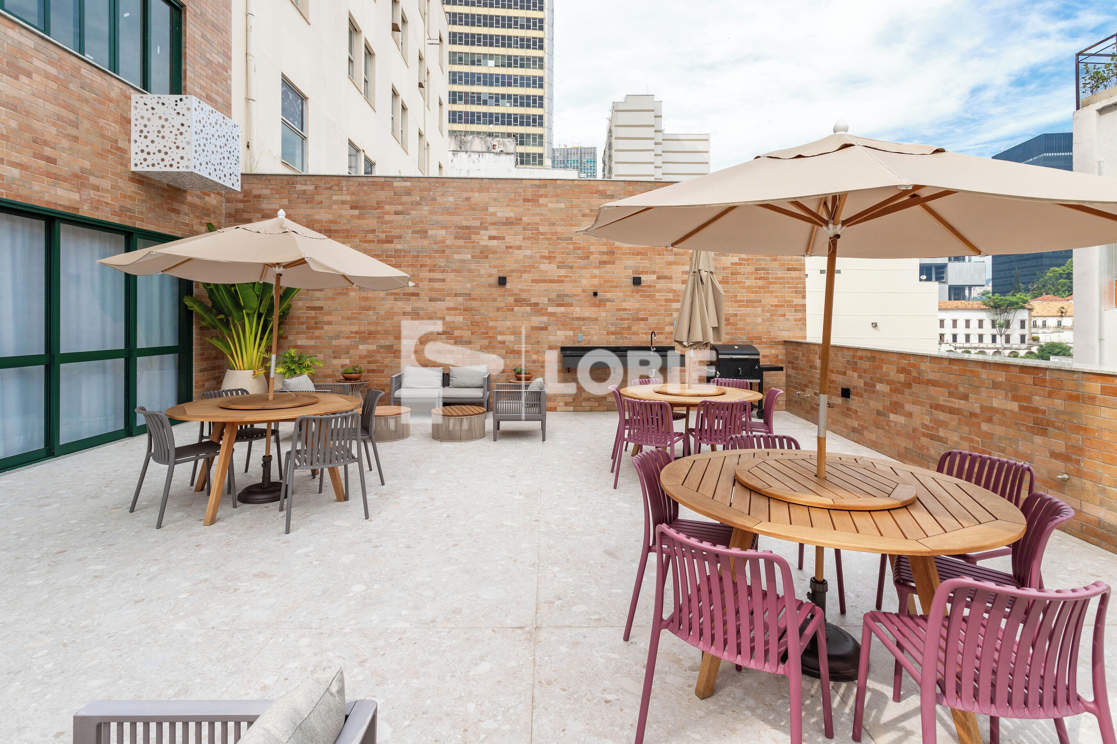 Ein Außenbereich mit einer Terrasse, bequemen Holztischen und -stühlen, beigen Sonnenschirmen und einer Ziegelwand im Hintergrund.