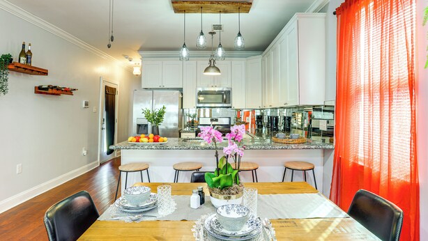 Cucina moderna con mobili bianchi, ventilatore a soffitto in legno, lampade a sospensione e isola centrale con lavello e ciotola di frutta.