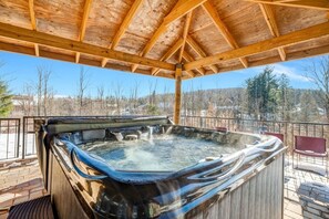 Ein Whirlpool unter einem Holzkiosk mit Blick auf Bäume und eine Brücke.
