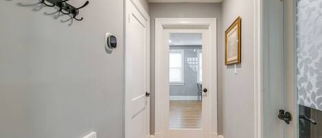 A hallway with a coat rack, a door with a peephole, and a framed picture on the wall.