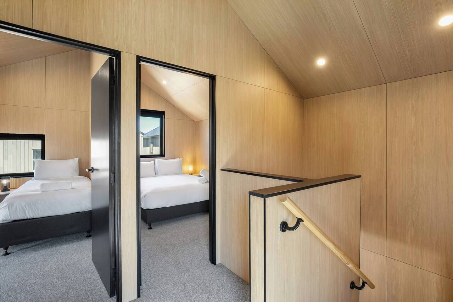A modern hotel room with a large bed, a separate sleeping area, and a wooden staircase.