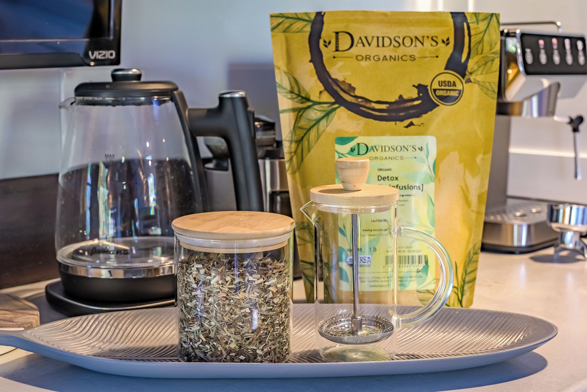 Eine Küchenarbeitsfläche mit Kaffeemaschine, einem Glasbehälter mit Holzdeckel und einer Packung Bio-Kaffee.