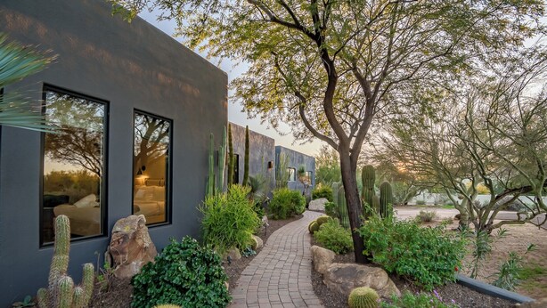 A modern building with large windows and a paved pathway leading to a garden with cacti and shrubs.
