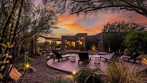 A modern outdoor patio with lounge chairs and a pool, surrounded by desert vegetation.
