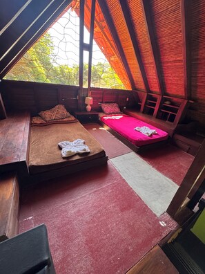 A cozy, rustic room with two beds, a wooden floor, and a view of trees through a window. - Cabuya Lodge (Cobano)