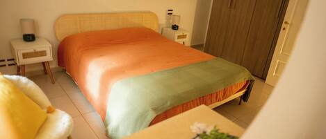 A neatly arranged bedroom with a bed, bedside tables, a chair, and a small table with a cup and a plate.