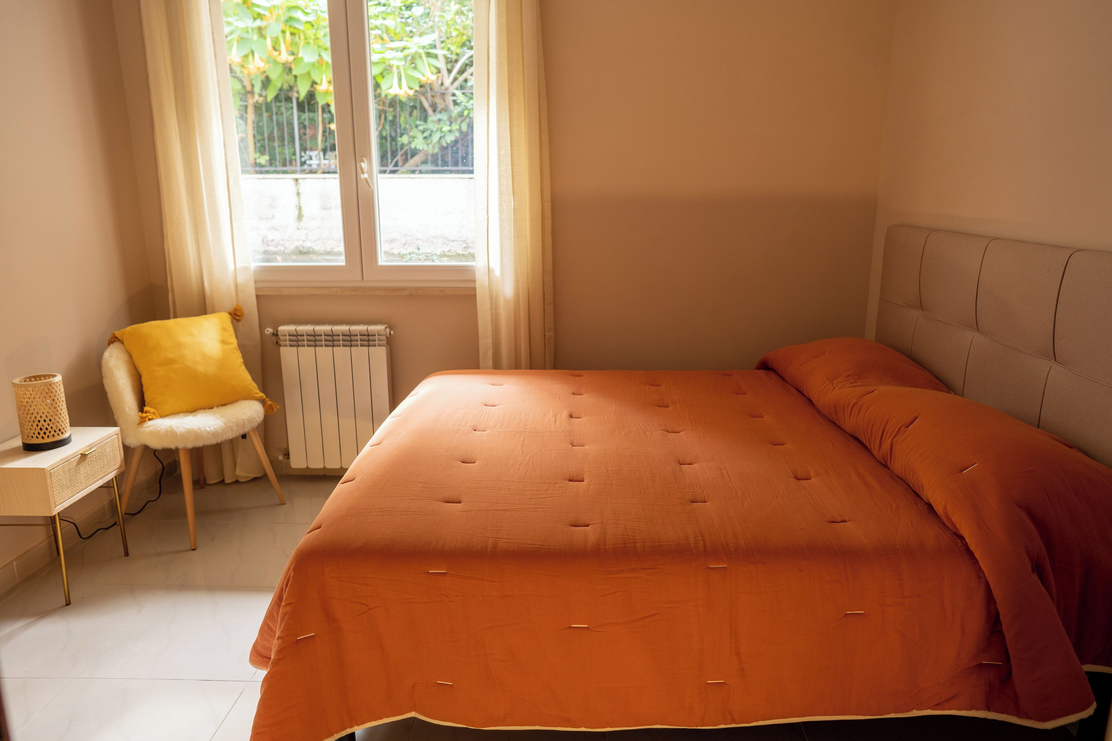 A bedroom with a large bed, a chair with a yellow cushion, and a radiator.