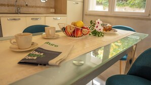 A dining area with a glass table, a bowl of fruit, a cup, and a menu. - NEW Charming 2-Bedroom Apartment in Private Roman Villa Oasis (Lazio)
