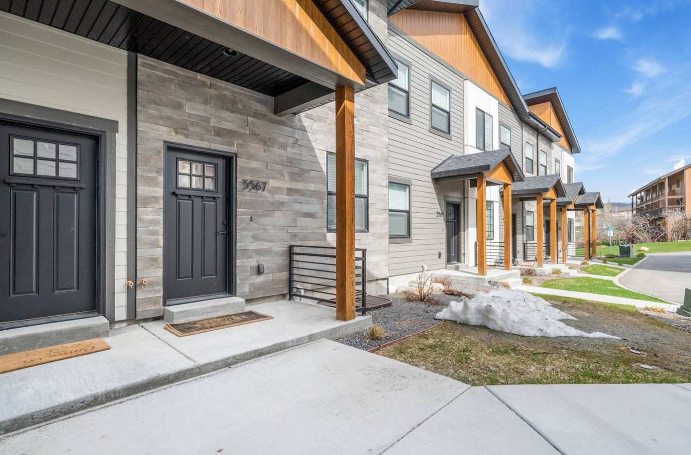 A modern residential building with a stone facade, black doors, and a well-maintained lawn.