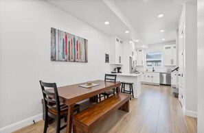 A modern kitchen with white cabinets, a wooden dining table, and a bench. - Lake view Townhouse | Private Hot Tub (Eden)